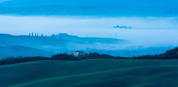 Vue horizontale d'un bâtiment isolé entouré d'arbres verts sur les collines dans une matinée brumeuse — Photo