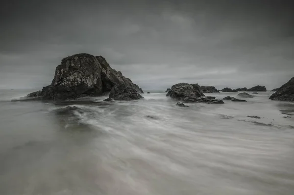 Belo tiro de formações rochosas no corpo de água com movimento fluente sob um céu cinza nublado — Fotografia de Stock