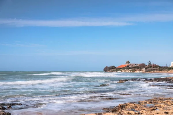 Tiro horizontal do belo mar com ondas loucas e uma casa na costa com um telhado vermelho — Fotografia de Stock