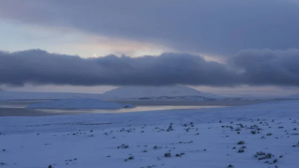 Szerokie ujęcie śnieżnego brzegu w pobliżu zamarzniętej wody pod zachmurzonym niebem — Zdjęcie stockowe
