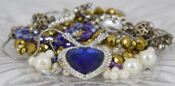 Closeup shot of a beautiful heart shaped blue emerald necklace lying on a pile of jewelry