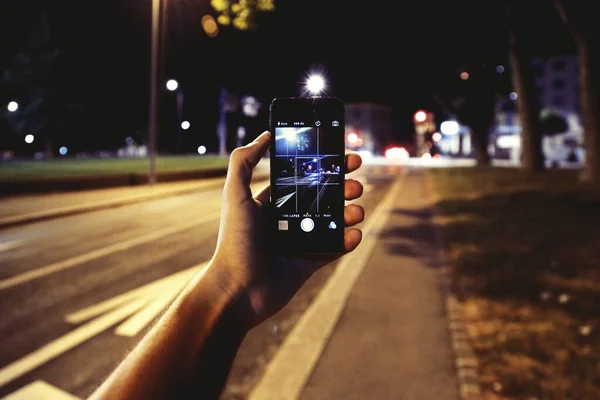 Persona con un teléfono inteligente tomando una foto de los hermosos edificios con luces en la noche — Foto de Stock
