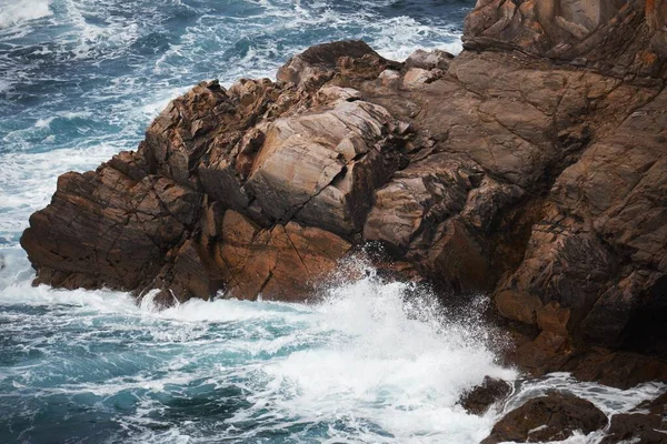 Primer plano de un acantilado rocoso cerca de un áspero cuerpo de agua con las olas salpicando las rocas — Foto de Stock