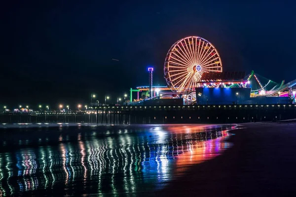 Fotografia noturna horizontal de uma praia de um parque de diversões com uma grande roda gigante — Fotografia de Stock