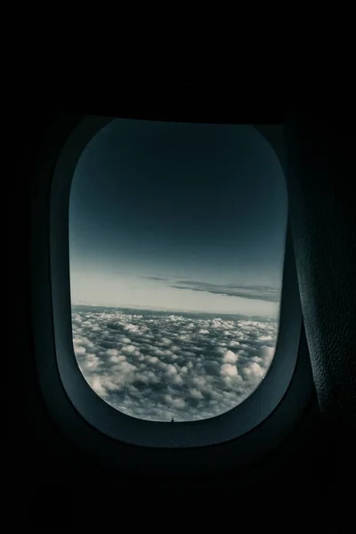 Vertical shot of an airplane window with the view of clouds and dark blue sky — 图库照片