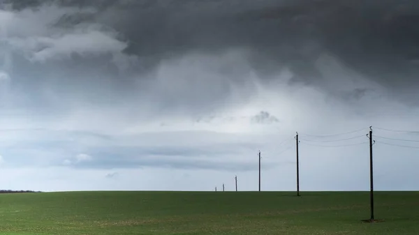 Vackra skott av tråd stolpar i en tom gräsbevuxen fält under en molnig himmel — Stockfoto