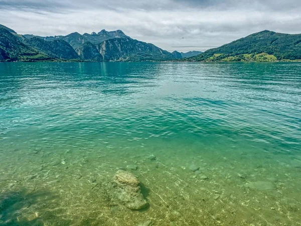 A beautiful shot of a crystal clear body of water with green mountains visible in the distance