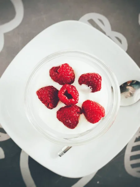 Вертикальний знімок смачного йогурту з червоними ягодами зверху біля срібної ложки на чорній поверхні — стокове фото