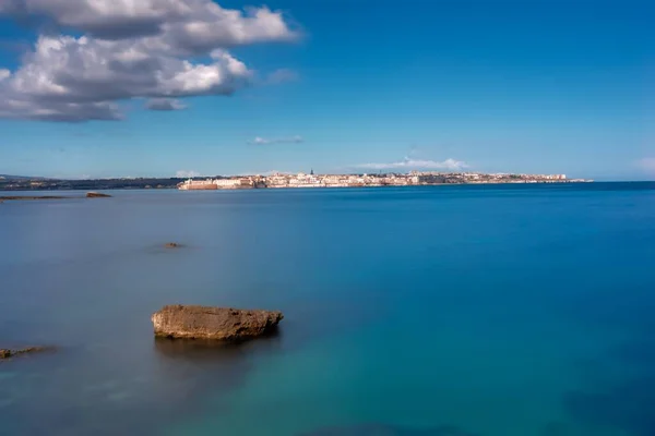 Gündüz vakti beyaz bulutların altında kaya oluşumları olan güzel mavi deniz — Stok fotoğraf