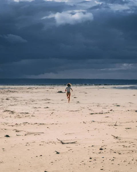 Vertikální záběr na pláž se ženou běžící pod zataženou oblohou — Stock fotografie