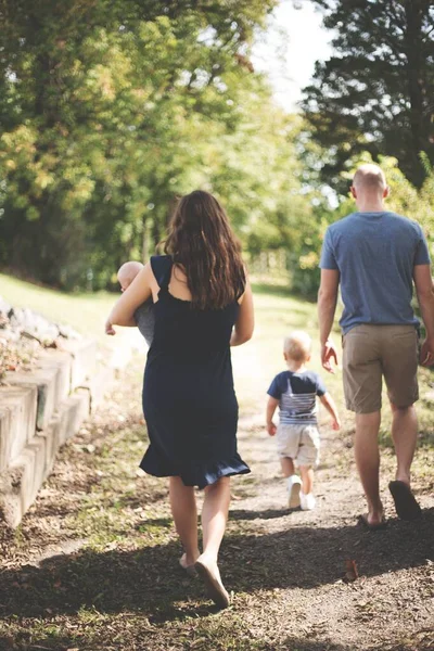 Vertikale Aufnahme einer Frau, die ein Kind hält und mit einem Mann und einem weiteren Kind im Park spazieren geht — Stockfoto