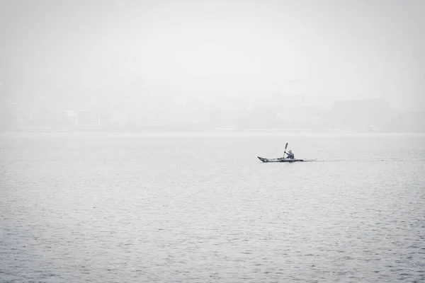 Horisontell bild av en person som paddlar på en båt på havet omgiven av dimma — Stockfoto