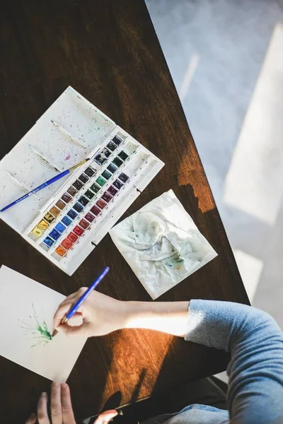 Overhead shot of a person painting with watercolors and a white watercolor palette. — Stock Photo, Image