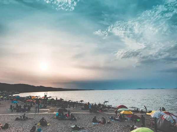 Silhouette di persone che riposano sulla spiaggia vicino al bellissimo mare sotto le nuvole mozzafiato — Foto Stock