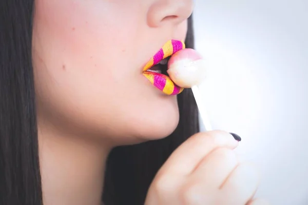 黄色とピンクのストライプの口紅を身に着けている女性のクローズアップショット食べますロリポップ — ストック写真