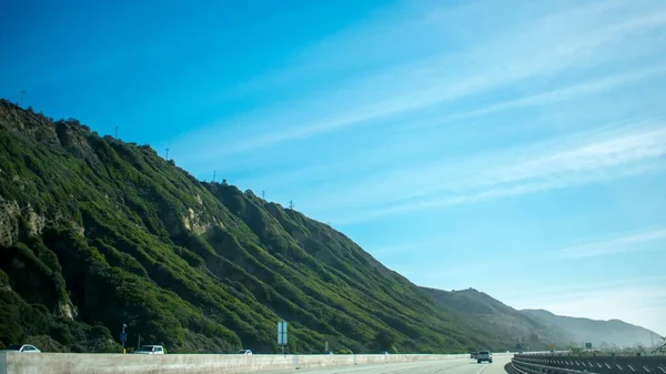 Landscape shot of a highway near beautiful green mountains during the day. — Stock Photo, Image