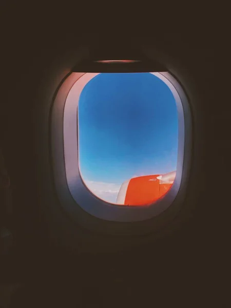 Крупним планом знімок крил літака, показаних через вікно з красивими хмарами на фоні Стокове Зображення