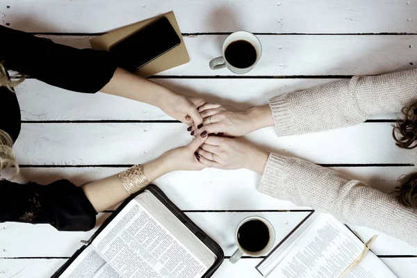 Foto aérea de hembras tomadas de la mano sobre la mesa con cafés y biblias abiertas —  Fotos de Stock