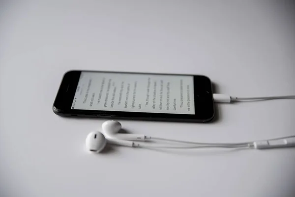 Colpo ad angolo alto della Bibbia su uno smartphone con cuffie su una superficie bianca — Foto Stock