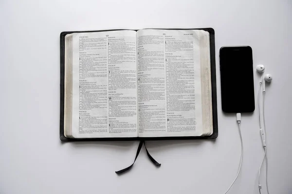 Overhead-Aufnahme einer geöffneten Bibel in der Nähe eines Smartphones auf einer weißen Oberfläche — Stockfoto