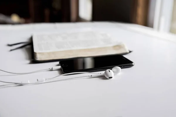 Nahaufnahme eines Smartphones und Kopfhörers auf einer weißen Fläche in der Nähe eines offenen Buches — Stockfoto