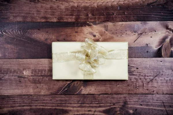 Overhead shot of a present with golden ribbon on a wooden surface — Stock Photo, Image