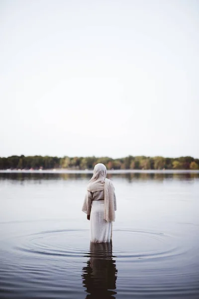 Plan vertical d'une femelle portant une robe biblique alors qu'elle marchait dans l'eau avec un fond flou — Photo