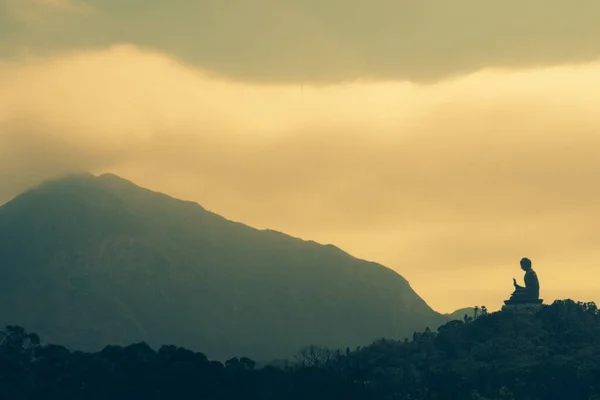 Silhouette di una statua sulla collina con una montagna in lontananza sotto un cielo nuvoloso — Foto Stock