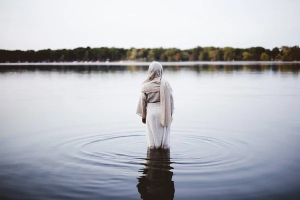 Female wearing a biblical robe and walking in the water shot from behind with a blurred background