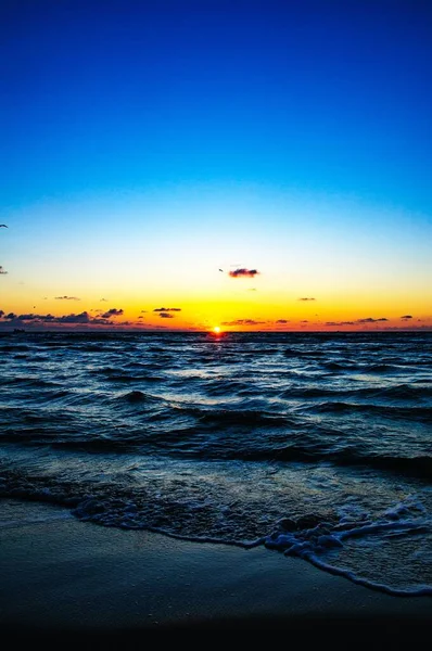 Pôr do sol sobre o oceano azul com pequenas nuvens no céu, criando a paisagem noturna perfeita — Fotografia de Stock