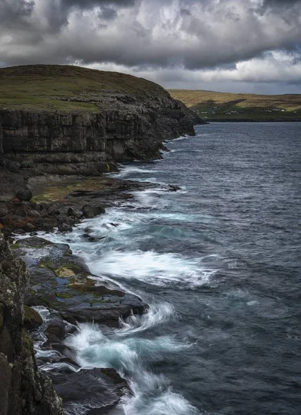 Vertical shot of sea waves hitting the shore under a blue cloudy sky — ストック写真