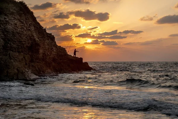 Girato di un maschio in piedi su una roccia cattura di pesce in mare calmo durante il tramonto — Foto Stock