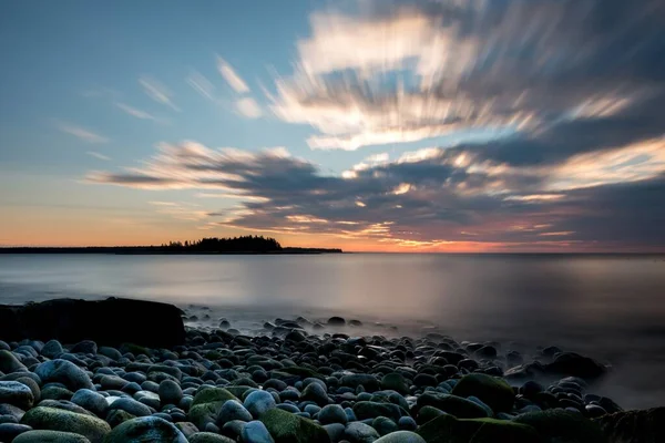 Pihentető jelenet egy tengerparton a felhős ég alatt és a nap lenyugvása a háttérben — Stock Fotó