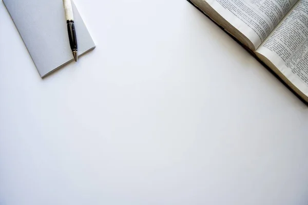 Tiro aéreo de uma bíblia aberta e um bloco de notas com uma caneta em uma superfície branca — Fotografia de Stock