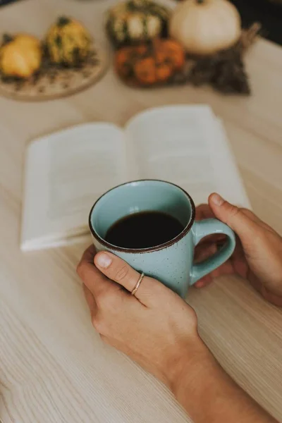 Plan vertical d'une femelle tenant une tasse de café avec un livre et quelques citrouilles en arrière-plan — Photo