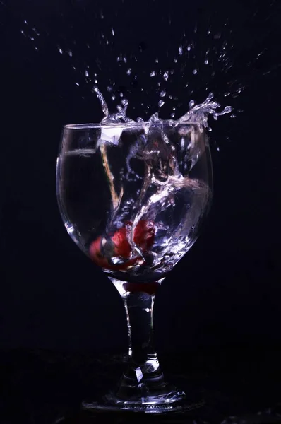 Verticaal schot van een glas water met een aardbei spetterend in het water op een donkere achtergrond — Stockfoto