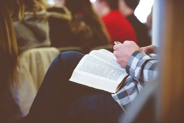 Nahaufnahme einer Person, die ihr Handy hält, während sie ein Buch mit verschwommenem Hintergrund liest — Stockfoto