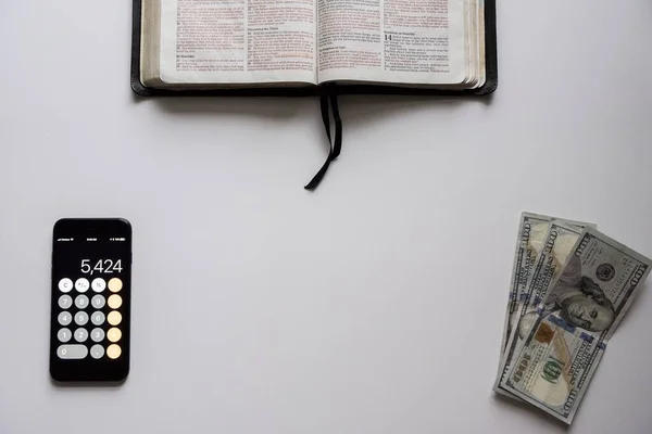Üzerinde para ve altta akıllı telefon olan açık bir İncil 'in resmi. — Stok fotoğraf