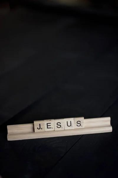 Vertical shot of wooden blocks spelling out Jesus on a black wooden surface — Stock Photo, Image