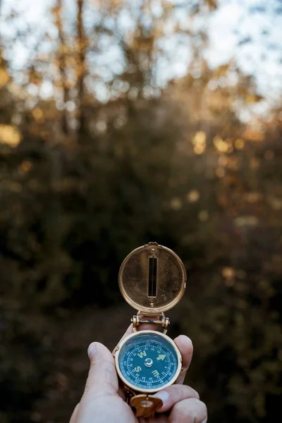 Vertical shot of a person holding a compass with a blurred natural background — 스톡 사진