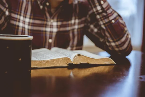 Primo piano di una persona seduta in un caffè e che legge la Bibbia con uno sfondo sfocato — Foto Stock