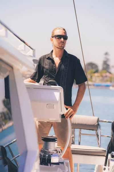 Vertical shot of a blonde male sailor with sunglasses on a white ship looking at the beautiful sea