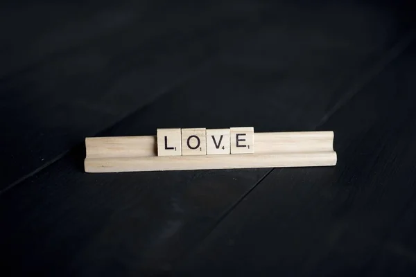 Primo piano colpo di blocco di legno spelling out amore su una superficie di legno nero — Foto Stock