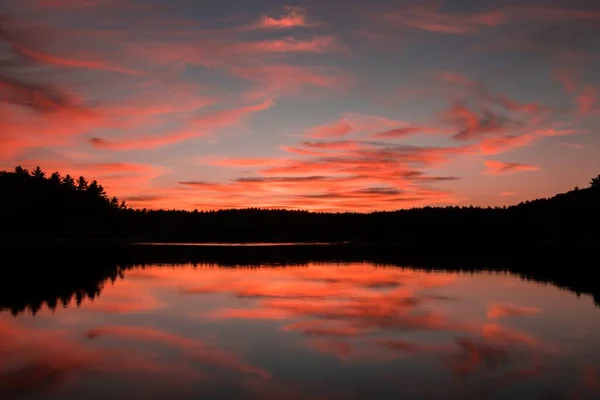 Ruhige Szene eines Sees mit dem Spiegelbild des Abendhimmels und einem dunklen Wald, der ihn umgibt — Stockfoto