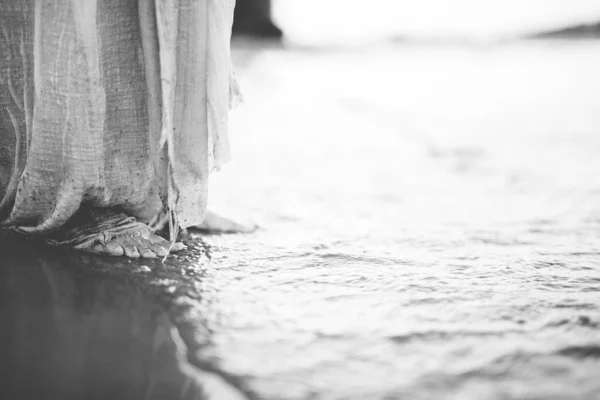 Closeup shot of a person wearing a biblical robe while standing on the shore in black and white — Stock Photo, Image