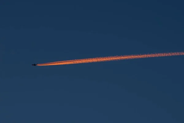 Прекрасная ночная сцена самолета, летящего высоко в небе и оставляющего за собой длинный оранжевый след — стоковое фото