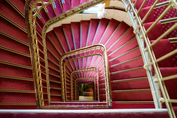 Foto de ángulo alto de una escalera de caracol rosa con asas doradas en un hermoso edificio —  Fotos de Stock