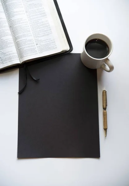 Overhead πλάνο ενός μαύρου ορθογωνίου σε μια λευκή επιφάνεια κοντά στη Βίβλο, καφέ και ένα στυλό — Φωτογραφία Αρχείου