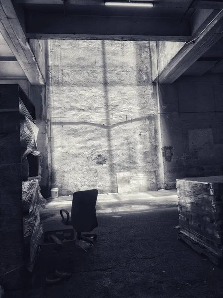 Grayscale tiro de uma cadeira de escritório isolado em um prédio abandonado com sombras perto de uma estante — Fotografia de Stock