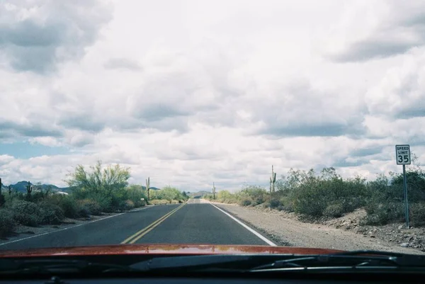 在多云的天空下，红色的车辆在一条被绿色植物环绕的高速公路上行驶 — 图库照片